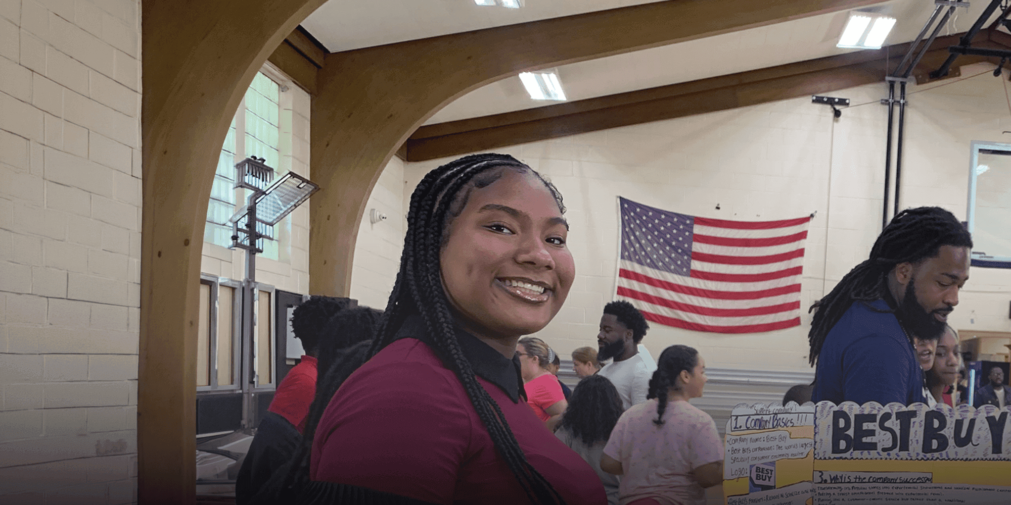 Smiling person at a student business project showcase in the school gym.