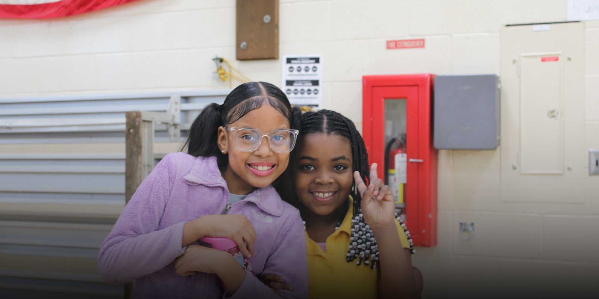 Two smiling students posing together, one making a peace sign.