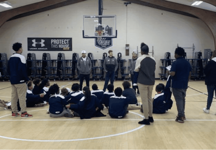 Adults addressing children sitting on a gymnasium floor.