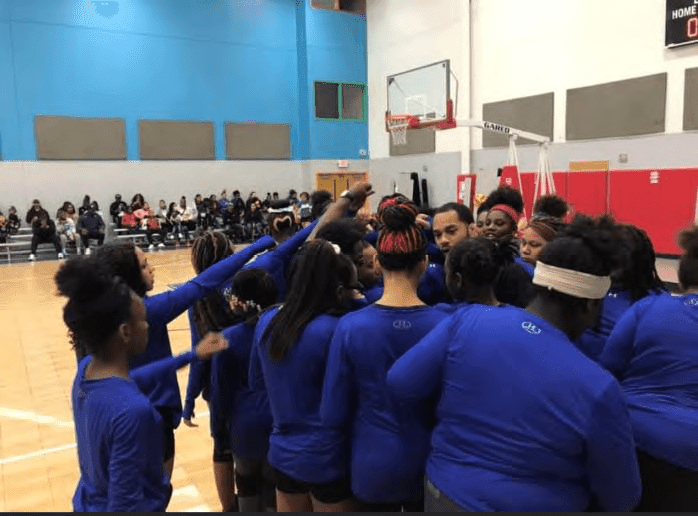 Adults in blue shirts huddle on a basketball court.
