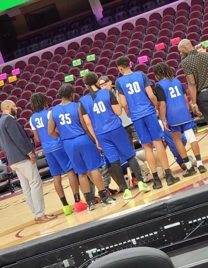 Basketball players in blue jerseys huddle on a court with two adults.