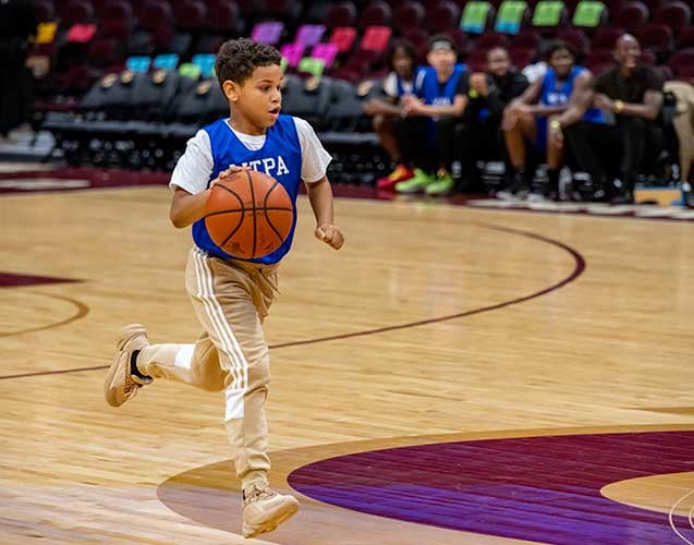 Child in blue jersey dribbling basketball on court.