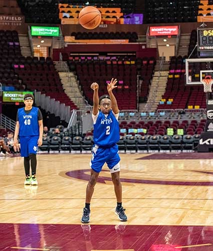 Child in blue jersey shooting basketball on court.