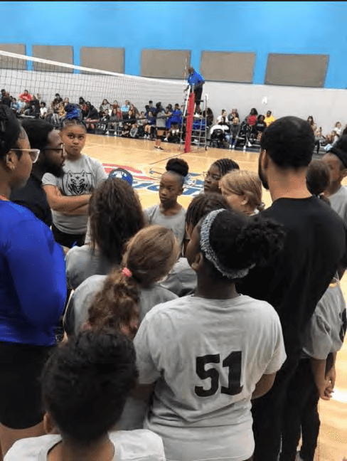 Children and adults gathered on a basketball court with a volleyball net.