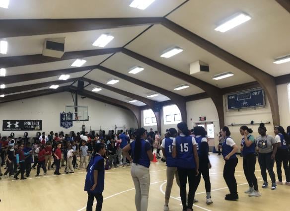 Children and adults in a gymnasium with a basketball hoop.