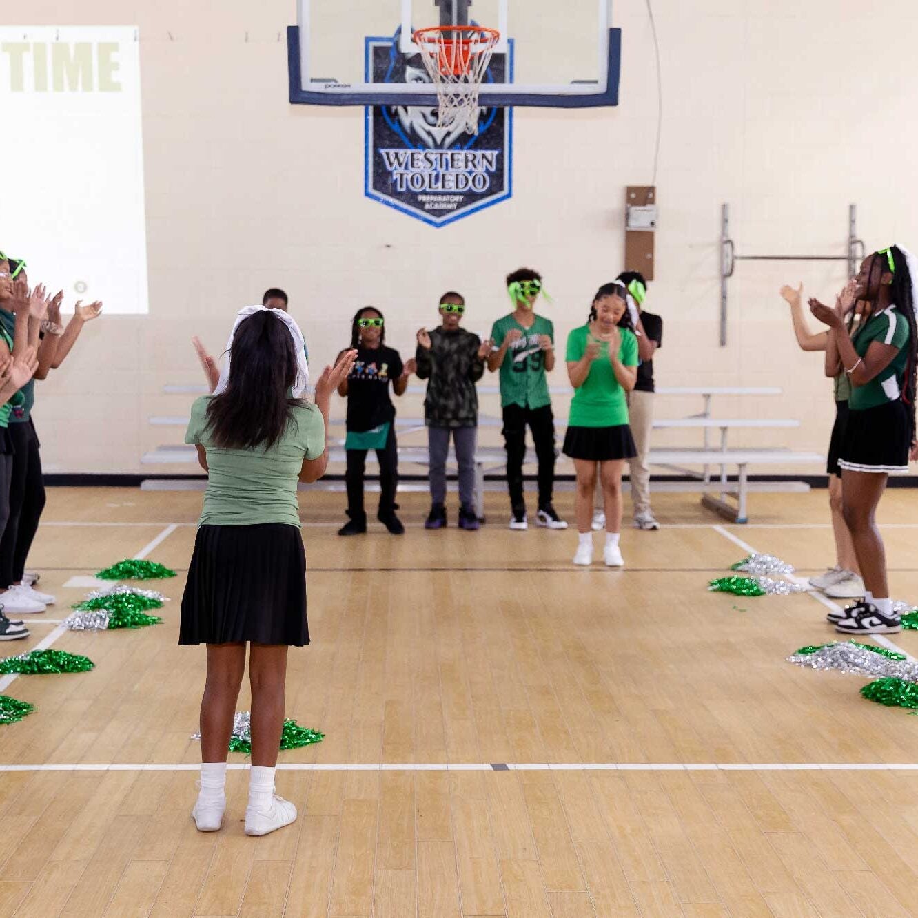 Children clapping in a gymnasium with pom-poms on the floor.