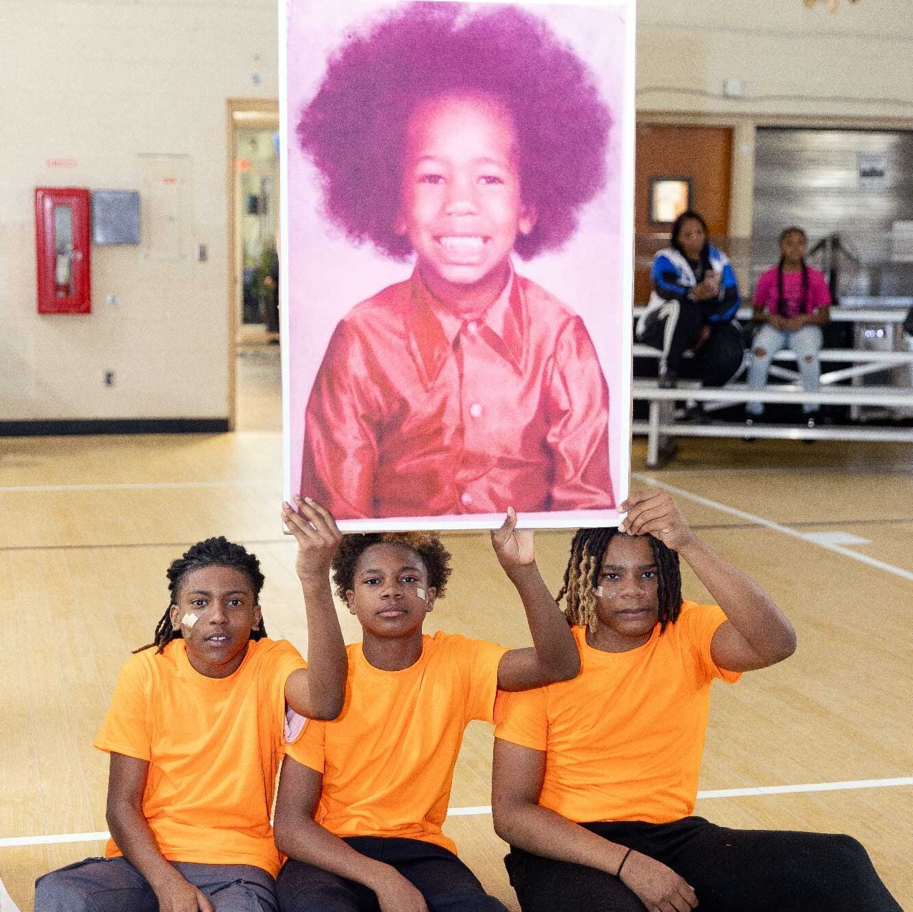 Three children hold up a large portrait of a smiling child.