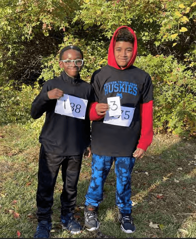 Two children smiling and holding race numbers.