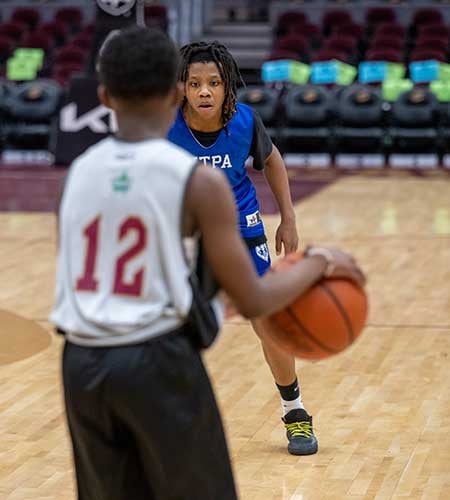 Two children playing basketball, one in white jersey, one in blue with ball.