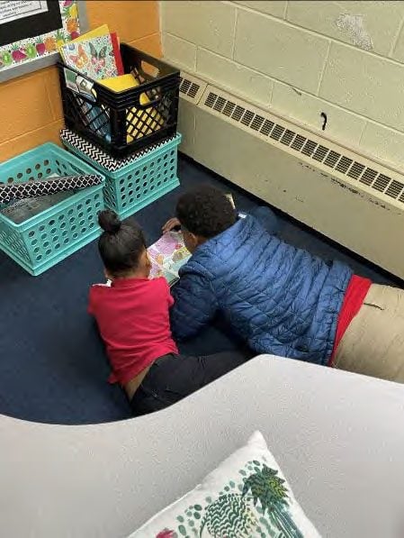 Two children lie on the floor, reading a book together.