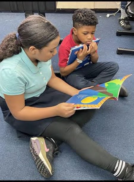 Two children sitting on the floor, reading books.