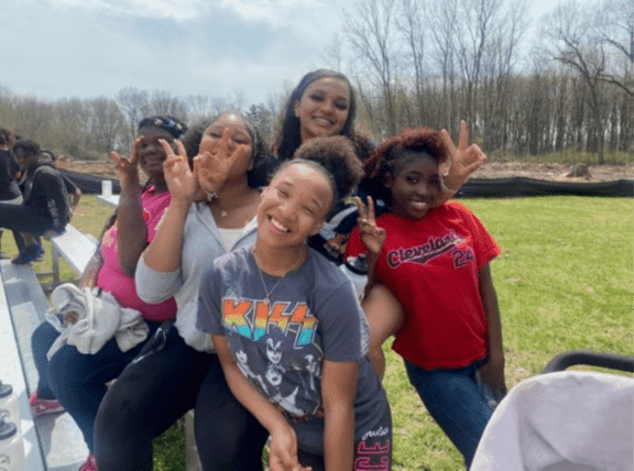 Five young adults smiling and making peace signs outdoors.