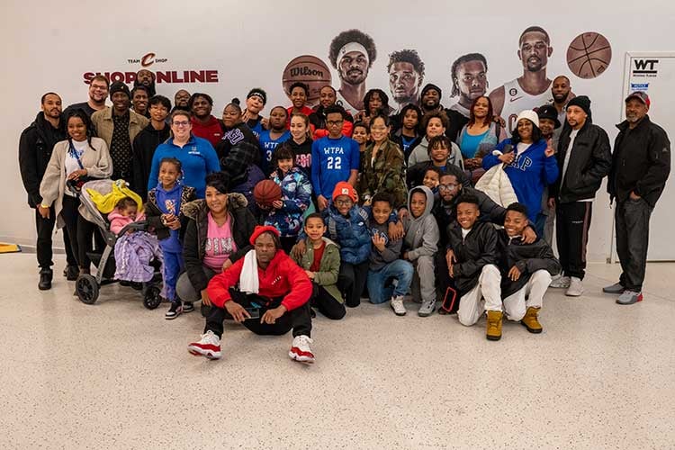 Large group of adults and children posing in front of basketball player murals.
