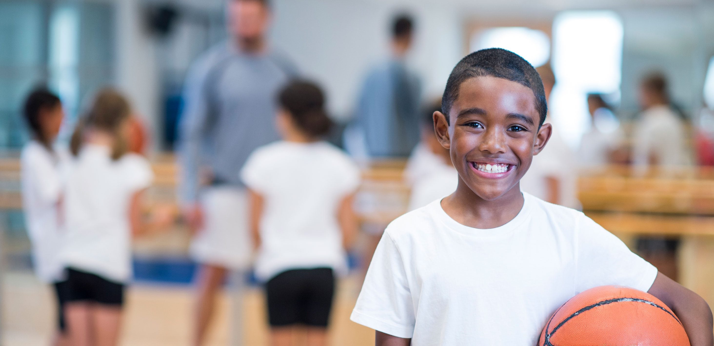Smiling child holding a basketball in a gym.