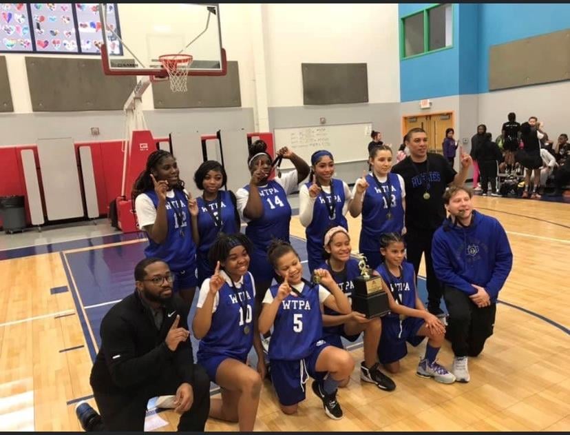 Youth basketball team with trophy and medals on court.
