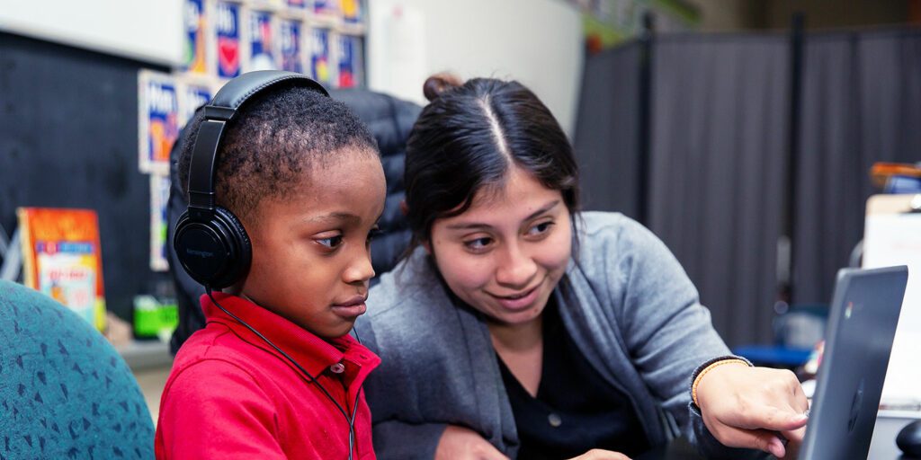 Teacher helping a student at a desk.