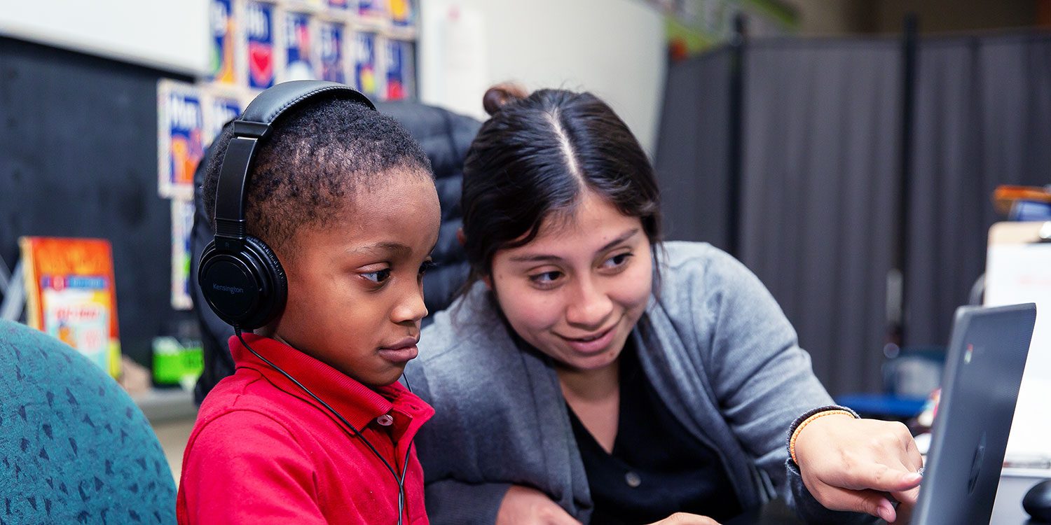 Teacher helping a student at a desk.